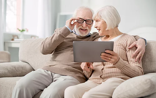 Älteres Paar sitzend auf der Couch mit Brille und Tablet