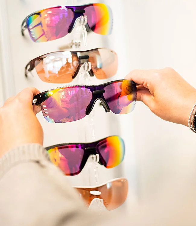 Person nimmt eine Sportbrille aus einem Brillenaufsteller mit fünf Brillen heraus